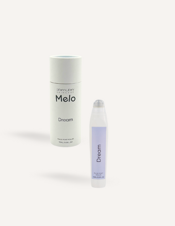 A cylindrical container labeled "Melo Dream" sits beside a small oil roller bottle with a purple label that reads "Melo Pulse Point Oil Roller - Dream." Both items, ideal for a calming bedtime ritual with essential oils, are set against a plain white background.