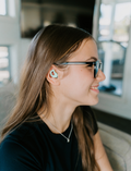 Teenage girl with glasses wearing a teal Curvd Earplug from The Play Way, smiling, experiencing improved sensory focus.
