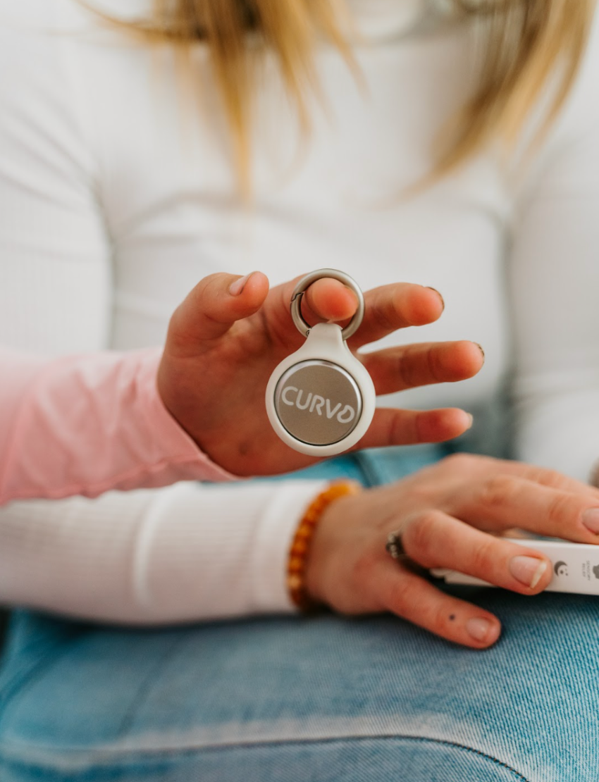 Hands hold a white Curvd earplug case on a keychain from The Play Way, ideal for portable sensory regulation.