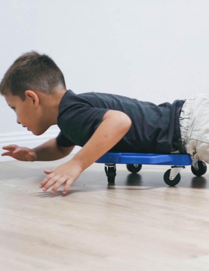 Young boy using The Play Way scooter board, a therapist-developed tool for promoting core strength and coordination in play.
