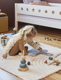 Young child playing with wooden toys, including an airport set and stacking rings, on a rug.