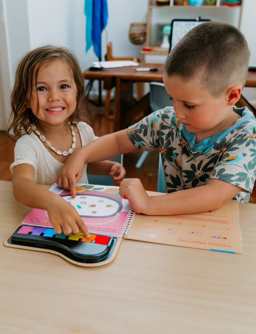 The Therapy At Home Fine Motor Foundations Program features a teal box with colorful shapes, filled with paint sets, coloring books, crayons, markers, stickers, stamps, and a red drawstring bag—ideal for boosting children's fine motor skills.