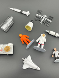 Collection of space-themed miniature figures including astronauts, rockets, and the ISS on a dark background.