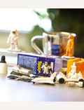 Close-up of safari space figures: astronauts, shuttle, rover, and monkey, arranged on a table with a mug.
