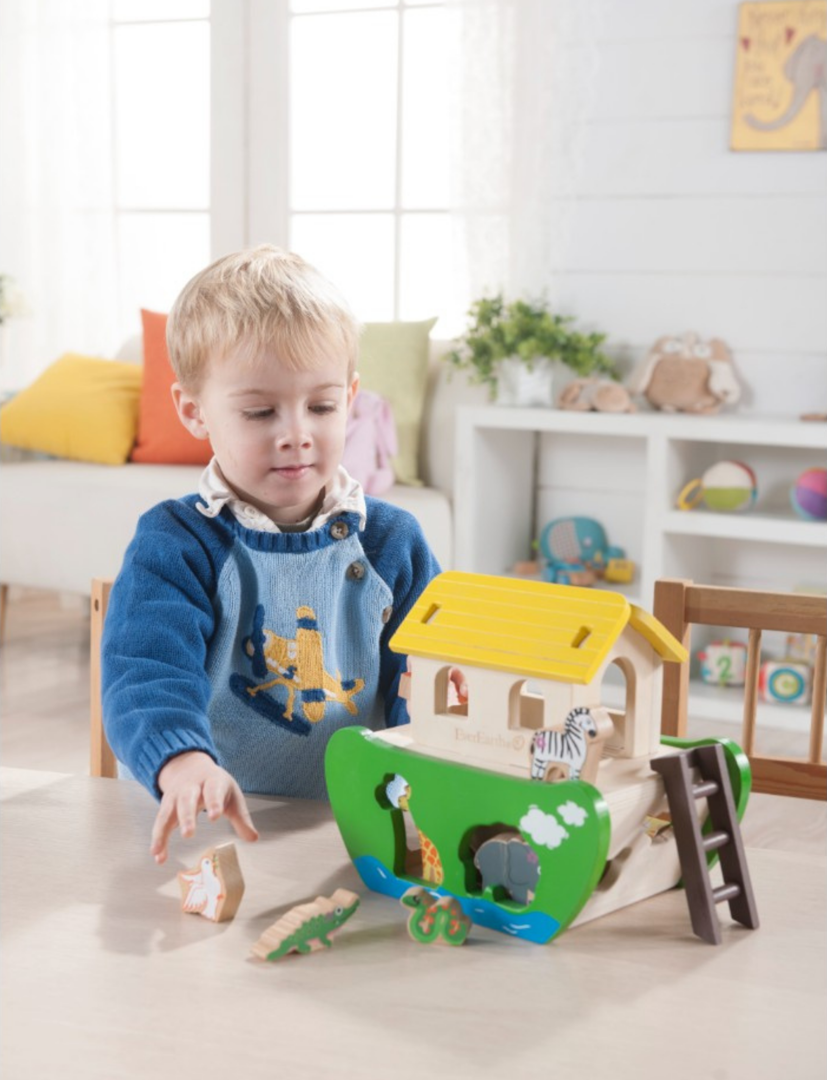 Boy playing with a wooden Noah's Ark shape-sorting toy, placing animal figures on the ark.