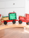 Two Connetix magnetic tile train cars, one red with black wheels, carrying colorful magnetic tiles, on a wooden surface.