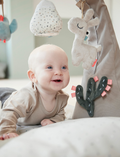 Smiling baby lying under a grey activity gym with plush llama, bird, and cactus toys