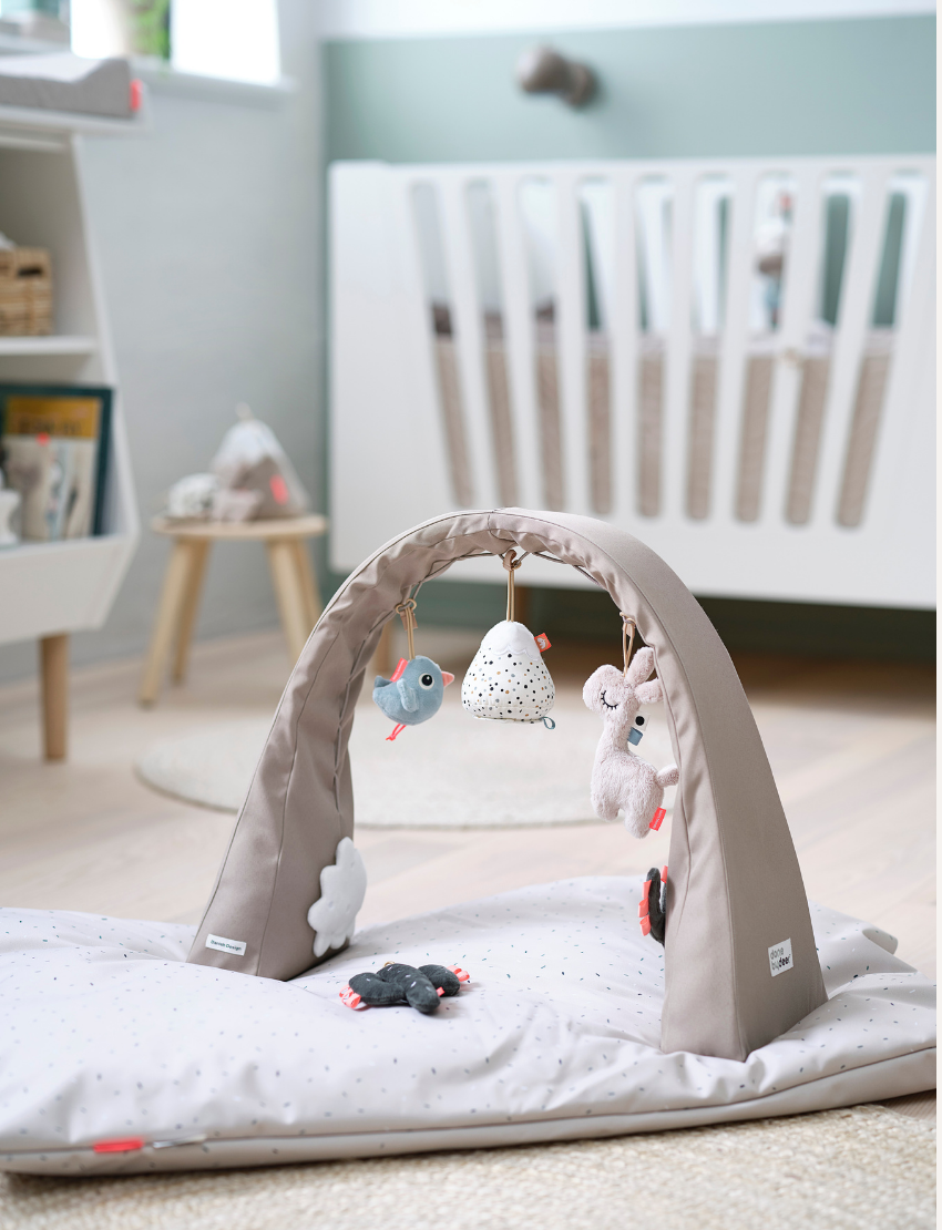 Grey activity gym set up on a play mat in a nursery with baby and toys