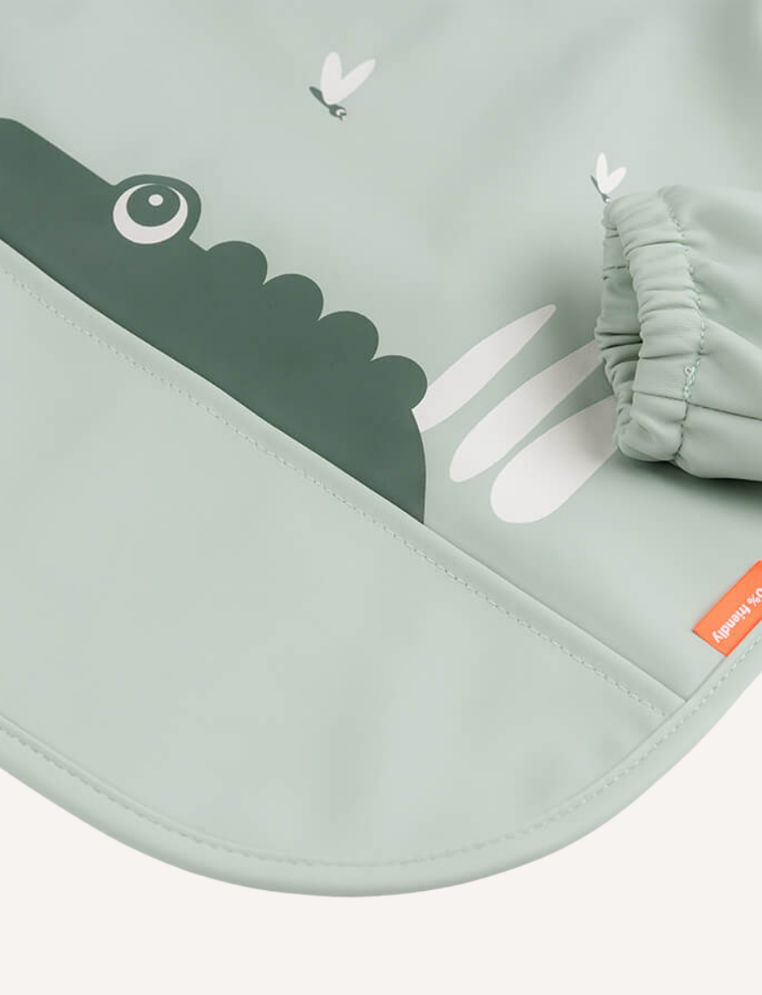Sage green baby bib with green crocodile graphic and elasticated cuff. 100% friendly label.