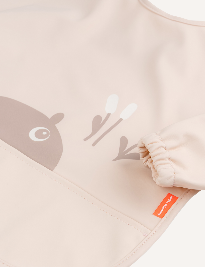 Powder pink baby bib with beige reindeer graphic and elasticated cuff. 100% friendly label.