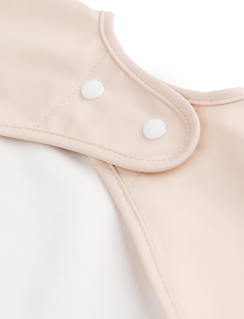 Close-up of powder pink baby bib with snap closure for neck fastening.