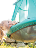 A happy young girl relaxing in a teal fabric swing seat outdoors.