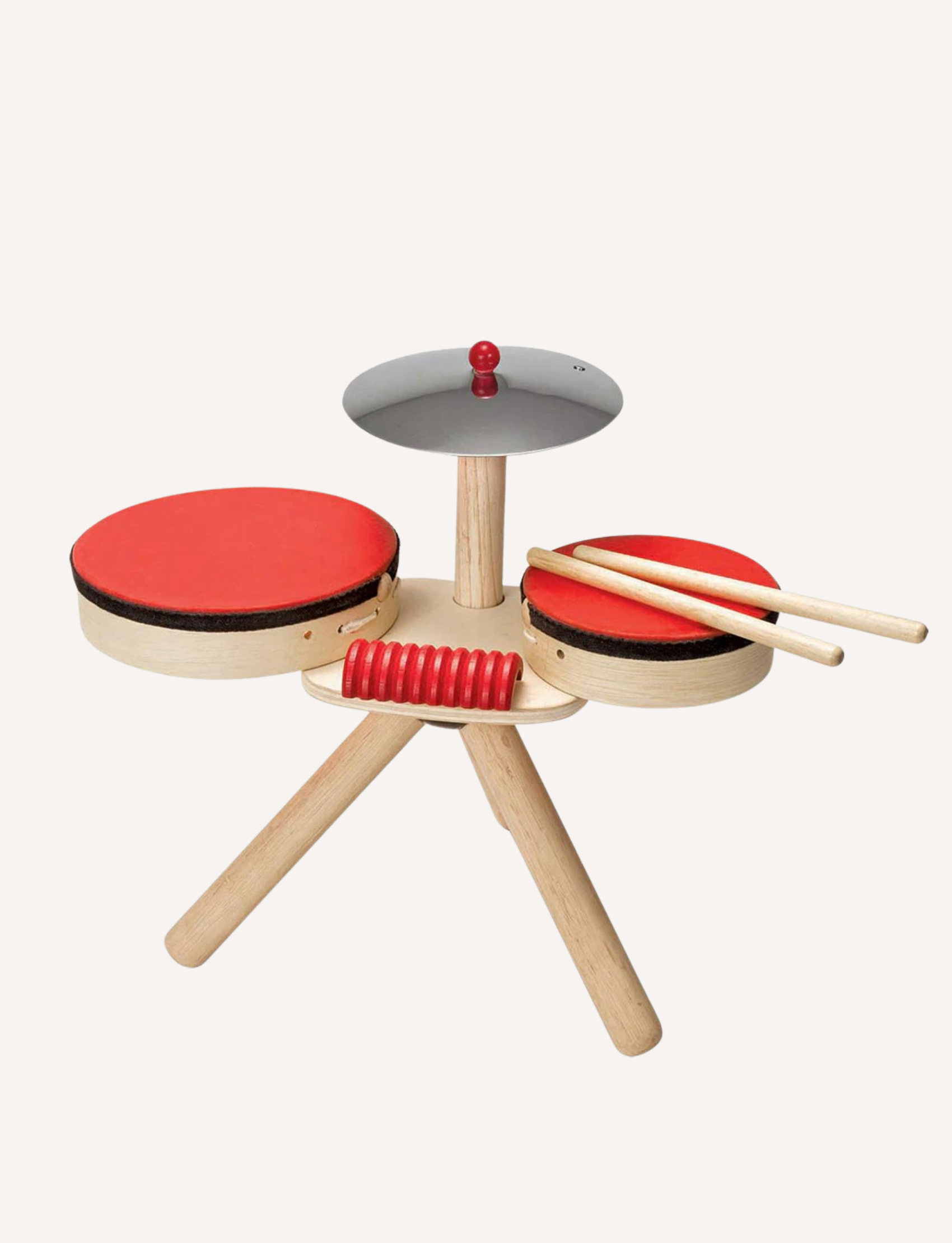 A small, portable wooden drum set with two red drums, a cymbal, and drumsticks, on a light background.