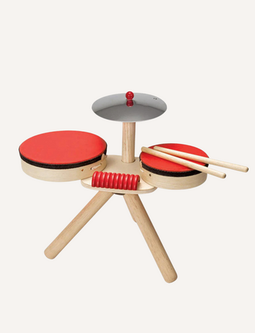 A small, portable wooden drum set with two red drums, a cymbal, and drumsticks, on a light background.