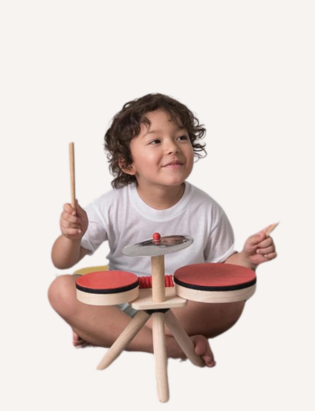 A small, portable wooden drum set with two red drums, a cymbal, and drumsticks, on a light background.