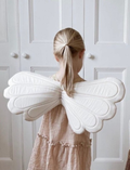 Back view of a young girl wearing a pale pink dress and large, fluffy white fairy wings.