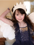 Smiling young girl dressed as a fairy with white wings and a gold crown, holding a wand.