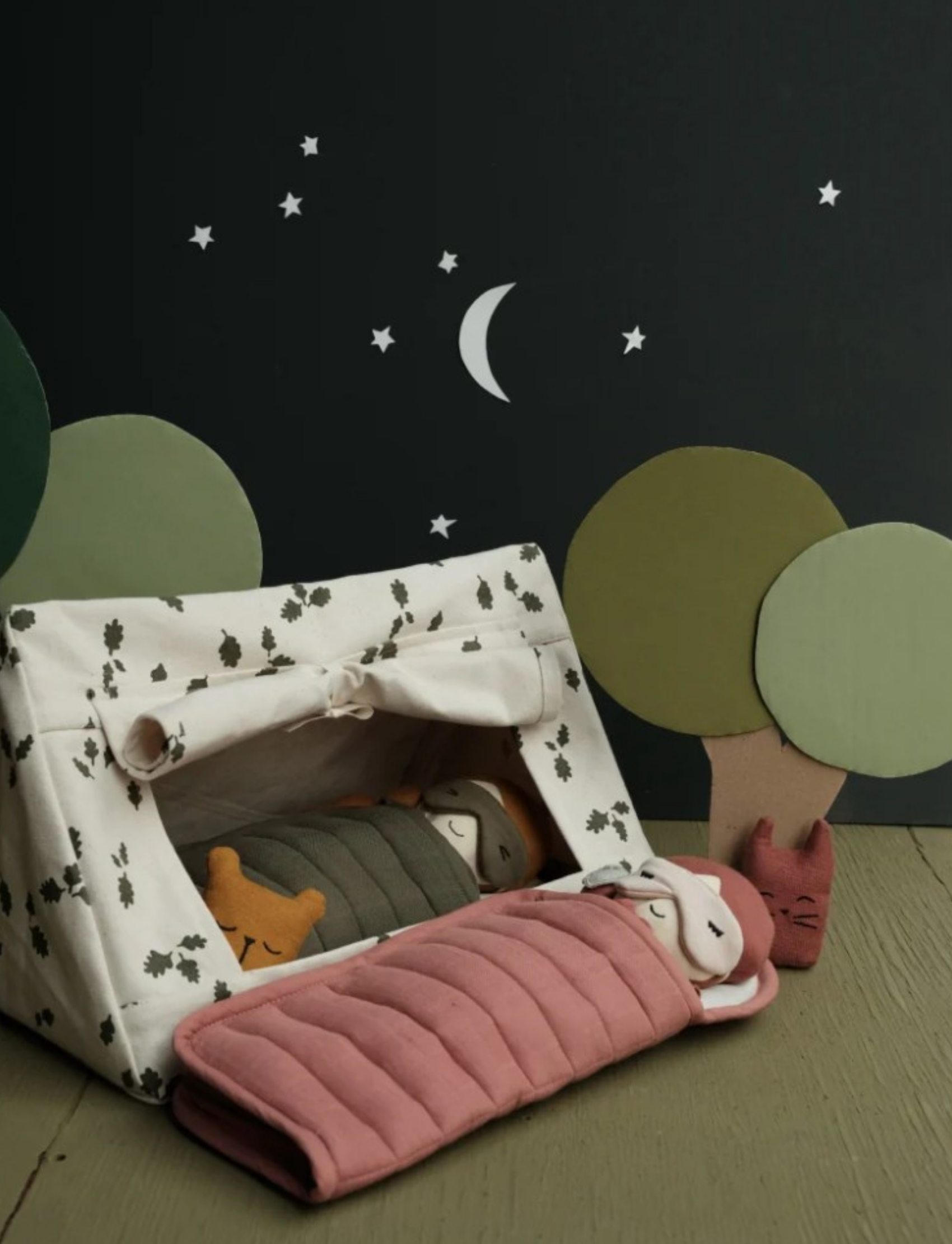 A camping scene with a patterned tent, dolls in sleeping bags, and stylized trees under a night sky.