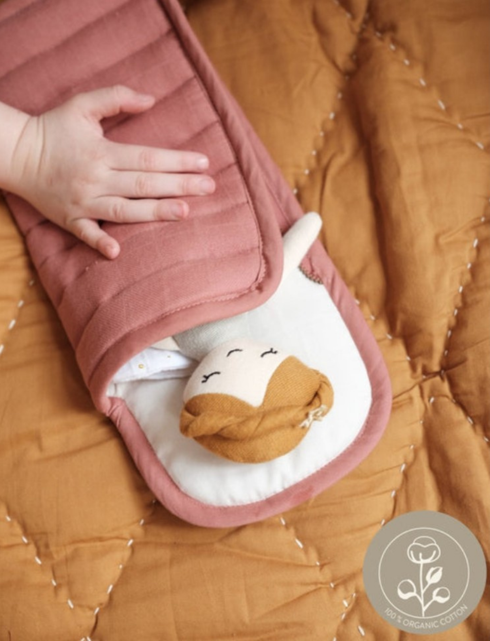 A child's hand tucking a doll into a pink quilted sleeping bag, close-up view.