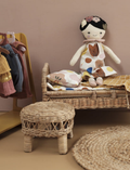 Plush doll 'Mei Mei' sitting on a doll bed with clothing on a rack nearby