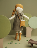 Plush doll with braided hair and brown dress, holding a sprig of greenery