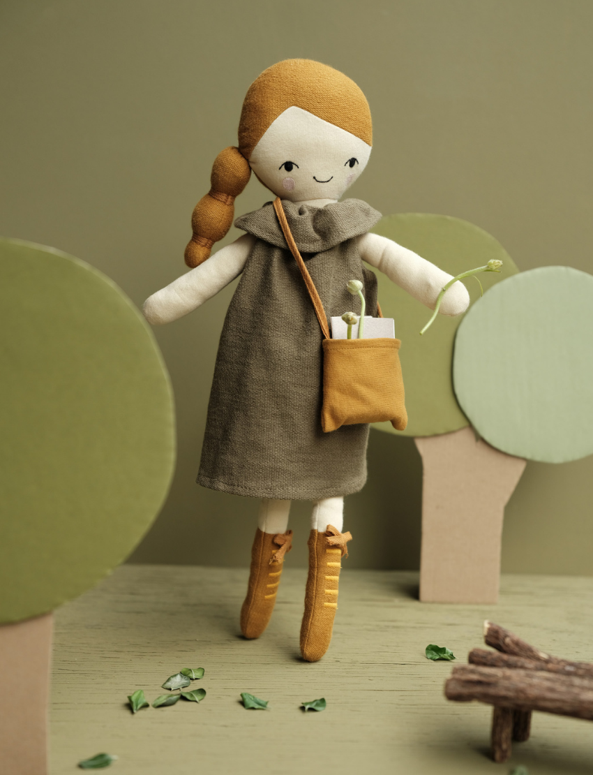 Plush doll with braided hair and brown dress, holding a sprig of greenery