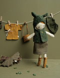Soft fabric doll with forest-themed clothing and accessories, including a bat toy hanging on a line.