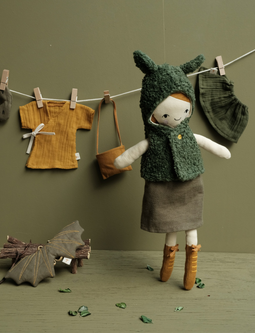 Soft fabric doll with forest-themed clothing and accessories, including a bat toy hanging on a line.