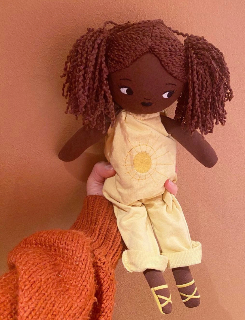 Child holding a plush doll 'Sol' with dark skin and textured pigtails