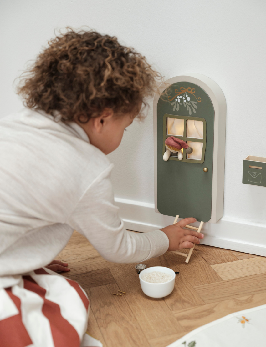 Child placing ladder at tiny Christmas elf door decorated with mistletoe.