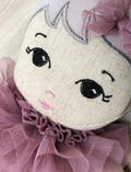 Detailed close-up of a fabric doll's embroidered face, featuring its eyes, nose, lips, and a ruffled tulle collar.