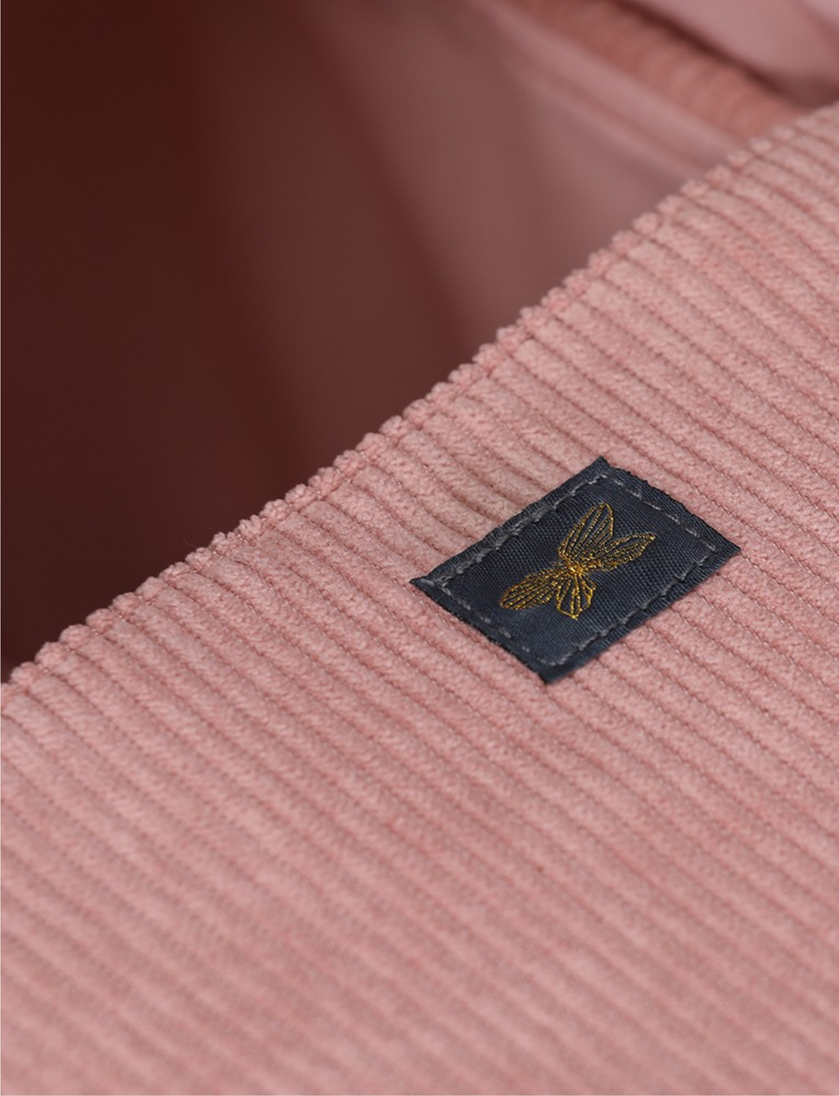 Close-up of a pink corduroy fabric with a small embroidered butterfly tag, detail from a doll carrycot.