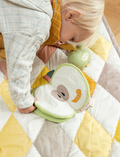 Toddler playing with a soft fabric apple book on a quilted mat, with a plush toy nearby.