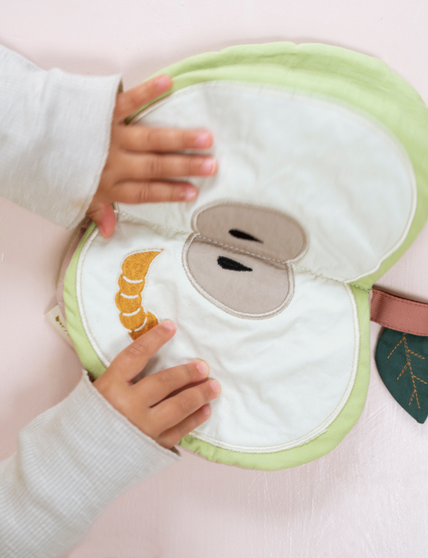 Soft fabric apple book opened by a child's hands, showing a worm and seeds.