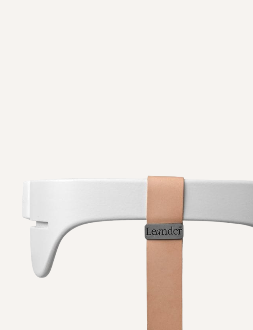 Close-up of a Leander high chair safety bar in white with a leather strap and branding.