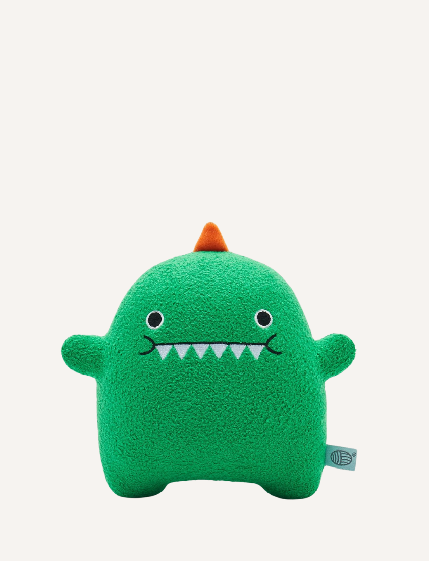 Green plush dinosaur toy with embroidered face, orange spikes, and a small brand tag.