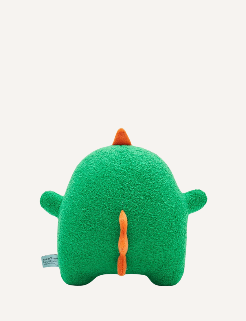 Green plush dinosaur toy with embroidered face, orange spikes, and a small brand tag.