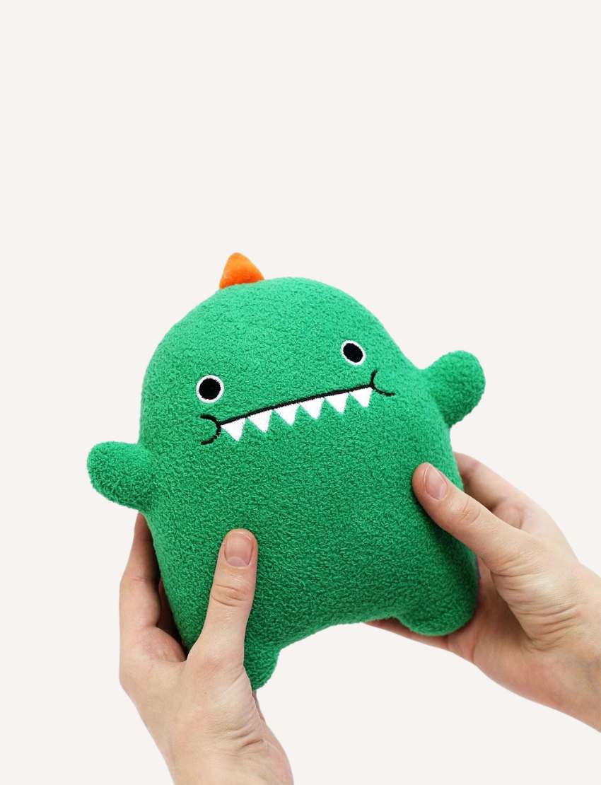 Green plush dinosaur toy held by hands, featuring cute embroidered face and orange spikes.