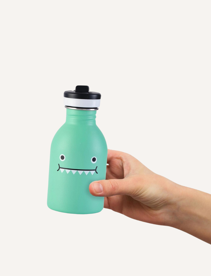 A hand holds a turquoise stainless steel water bottle with a cute dinosaur face design.