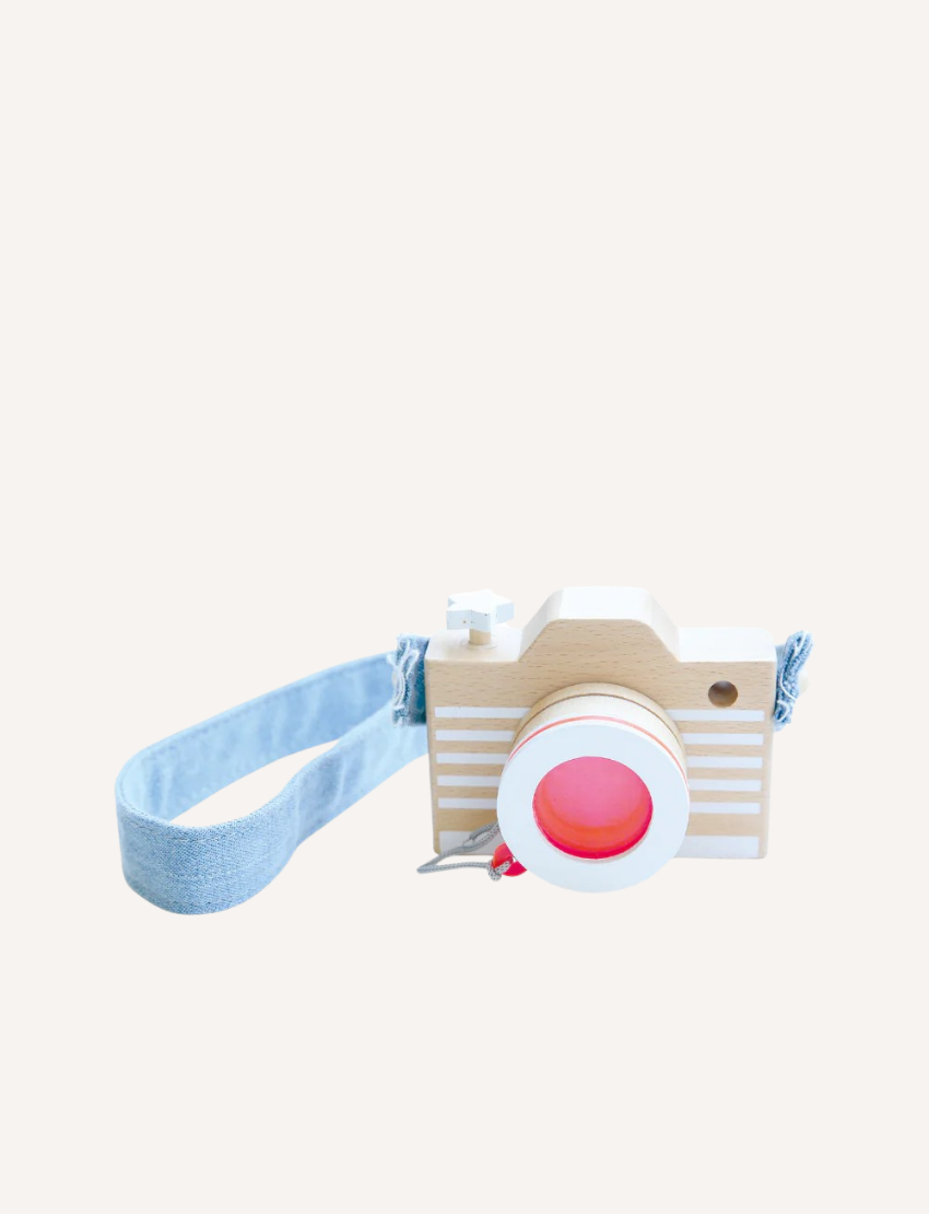 A wooden toy camera with white stripes and a pink lens, featuring a light blue denim strap.