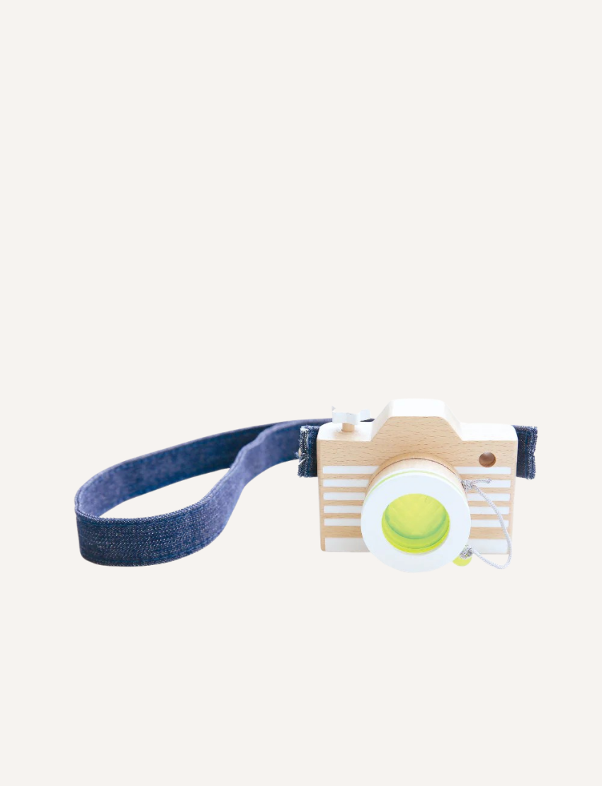 A wooden toy camera with white stripes and a pink lens, featuring a light blue denim strap.