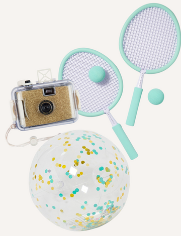 A flat lay image featuring the SunnyLife Mini Bundle by Sunnylife, including a transparent toy camera filled with glitter, two mint green badminton rackets with balls, and a clear inflatable beach ball brimming with colorful confetti.
