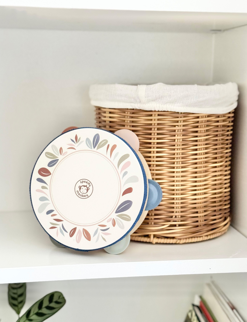 Speedy Monkey tambourine placed on a white shelf next to a woven basket, showcasing its design.