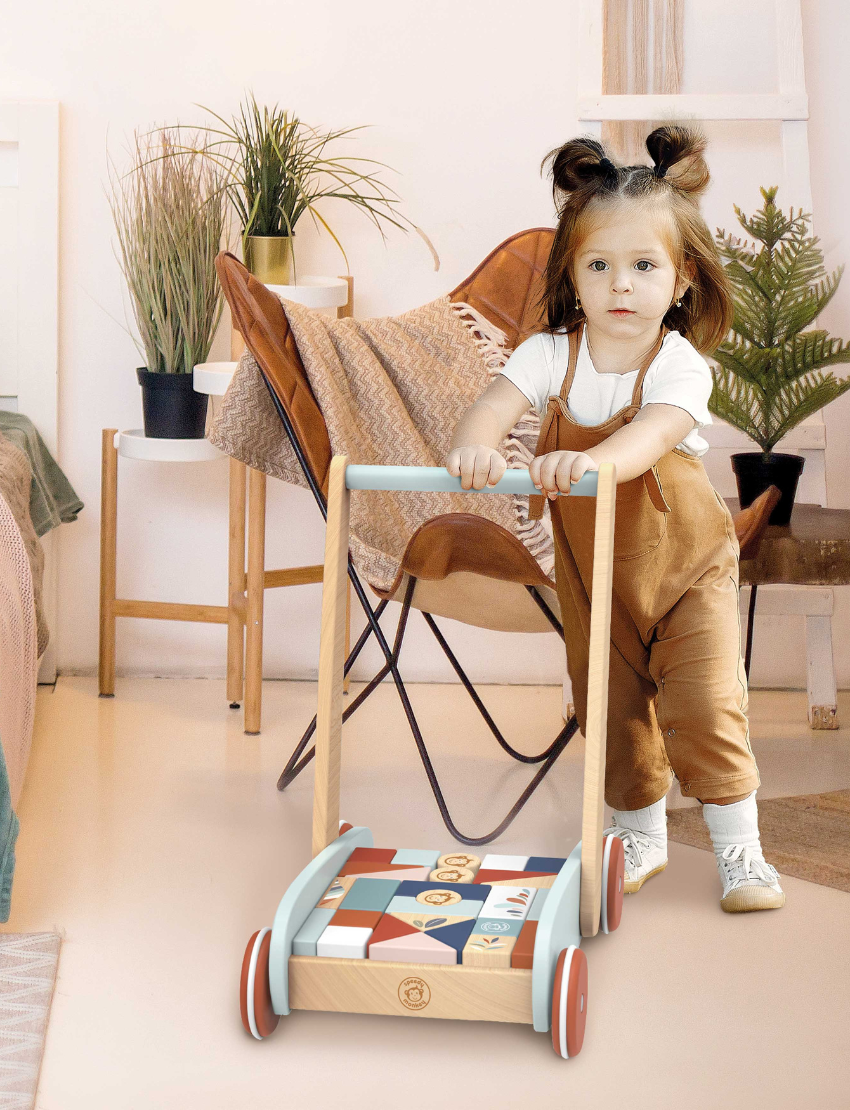Little girl in overalls playing with a wooden block walker filled with colorful geometric shapes.