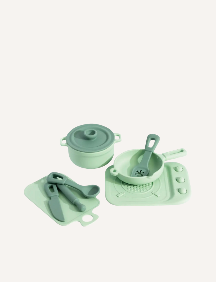 A complete green silicone kitchen playset featuring a pot, pan, stove, cutting board, knife, spoon, and spatula. BPA-free for kids.
