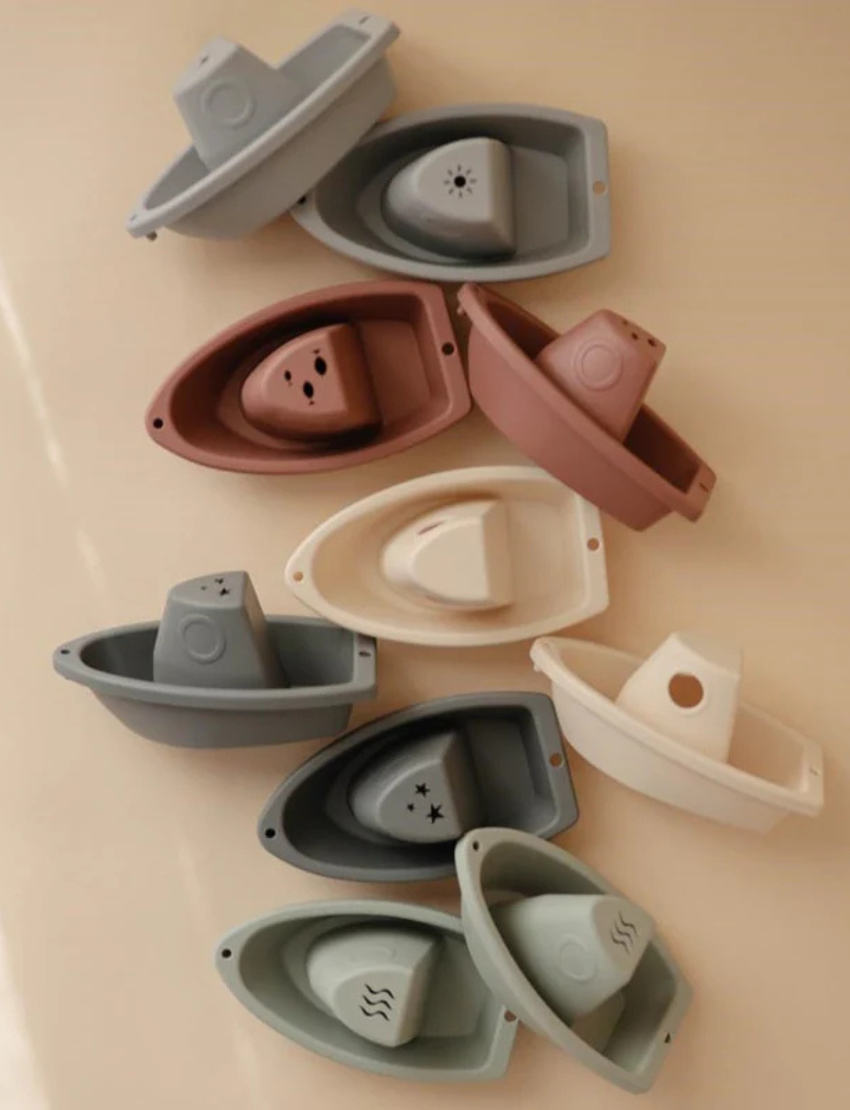 Stack of five pastel-colored nesting boat bath toys for kids, with a removable top piece, perfect for water play.