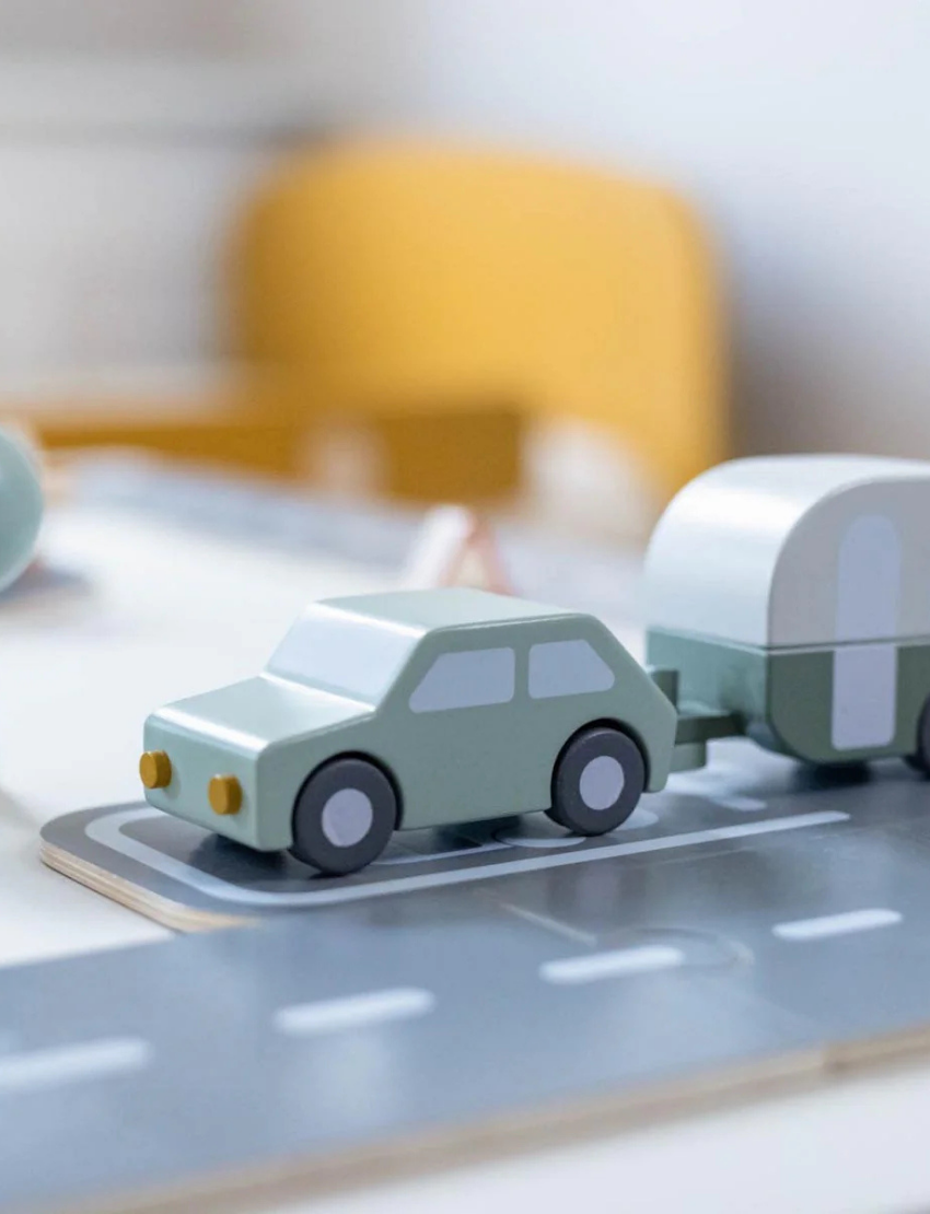 Close-up of a wooden toy car towing a caravan on a toy road.