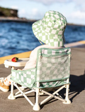 Baby in a green and white checkered bucket hat and matching portable high chair, perfect for outdoor mealtimes.