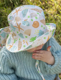 Adorable baby wearing a white bucket hat with vibrant seashell and starfish patterns, perfect for sun protection and summer adventures.