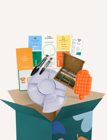 The Play Way Food Exploration Kit box overflowing with Food Creation Cards, tongs, spoons, Pop It toy, and a divided tray. Tools for children to explore food.